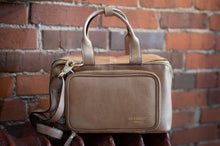 Load image into Gallery viewer, Beige handbag with a strap held against a brick wall
