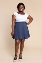 Load image into Gallery viewer, Woman wearing a white top and blue skirt against a beige background