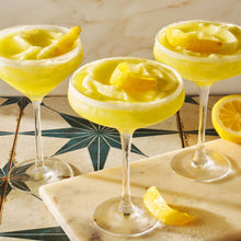 Load image into Gallery viewer, Three yellow cocktails with lemon slices in glass cups on a marble surface.