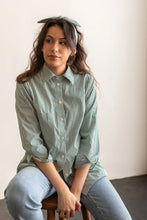 Load image into Gallery viewer, Woman wearing a green striped shirt and light blue jeans sitting on a stool.
