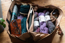 Load image into Gallery viewer, Brown leather bag filled with yarn, knitting supplies, and books on a wooden surface
