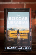 Load image into Gallery viewer, Book titled 'The Boxcar Librarian' by Brianna Labuskes on a wooden surface with a blurred brick wall background.