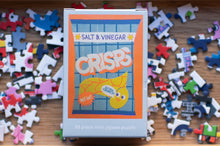 Load image into Gallery viewer, Salt & Vinegar Crisps puzzle packaging with scattered puzzle pieces on a wooden surface