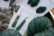 Green earrings on a card with yarn and stones in the background