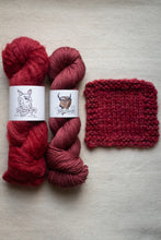 Load image into Gallery viewer, Two skeins of red yarn with labels and a knitted swatch on a beige surface