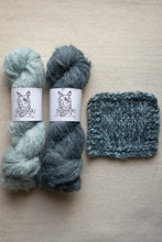Load image into Gallery viewer, Two skeins of yarn and a knitted swatch on a beige surface