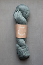 Load image into Gallery viewer, Skein of blue yarn with a label on a gray background