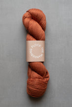 Load image into Gallery viewer, Skein of rust-colored yarn with a label on a gray background