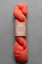 Load image into Gallery viewer, Peach-colored skein of yarn with a label on a gray background