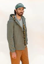 Load image into Gallery viewer, Man wearing a green jacket, cap, and brown pants on a white background