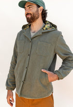Load image into Gallery viewer, Man wearing a green jacket with a hood and camouflage lining, standing against a plain background.