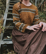 Load image into Gallery viewer, Person wearing a brown sweater with patterned sleeves and a long brown skirt, sitting on a wooden staircase.