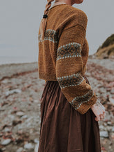Load image into Gallery viewer, Person wearing a brown knitted cardigan with patterned sleeves on a beach.