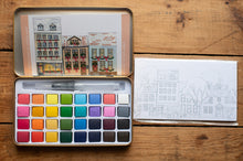 Load image into Gallery viewer, Watercolor paint set with a book of watercolor illustrations on a wooden surface