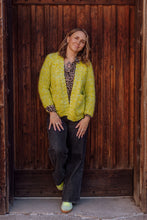 Load image into Gallery viewer, Woman wearing a bright green jacket standing against a wooden wall.