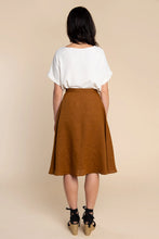 Load image into Gallery viewer, Woman wearing a white top and brown skirt against a beige background