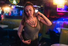 Load image into Gallery viewer, Woman with tattoos in a dimly lit bar setting