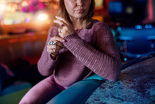 Load image into Gallery viewer, Woman sitting on a bench with a blurred city street background