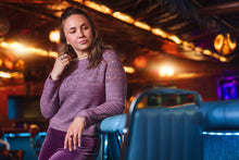 Load image into Gallery viewer, Woman in a purple sweater sitting in a dimly lit room with colorful lights.