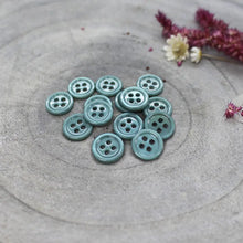 Load image into Gallery viewer, Teal buttons on a textured gray surface with flowers in the background