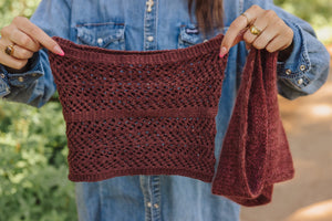 Person holding a maroon knitted garment against a blurred natural background