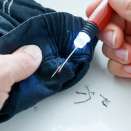 Person using a needle and thread with a light on fabric