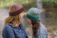 Two people wearing knitted hats by a body of water.