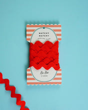 Load image into Gallery viewer, Red yarn with a striped packaging label on a light blue background