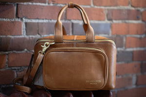 Brown leather bag with a visible brand logo against a brick wall.