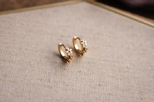 Load image into Gallery viewer, Pair of gold hoop earrings with floral details on a textured fabric background