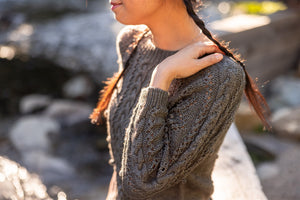 Person wearing a textured sweater with a blurred natural background