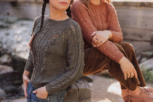 Two women wearing patterned sweaters sitting outdoors.
