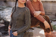 Two women wearing patterned sweaters sitting outdoors.