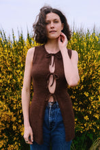 Load image into Gallery viewer, Woman wearing a brown sleeveless top with cut-out design in front of yellow flowers.