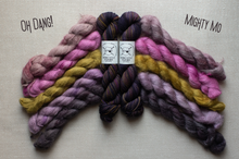 Load image into Gallery viewer, Four braided skeins of yarn arranged in a fan shape on a light beige fabric background. The yarn colors include dusty pink, lavender, mustard yellow, and dark purple with subtle orange and blue flecks.