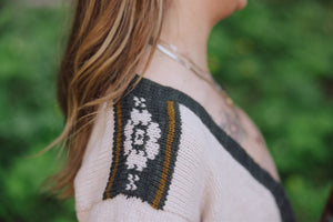 Close-up of a person wearing a sweater with a floral pattern on a blurred green background