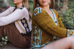 Two women sitting outdoors wearing patterned sweaters.
