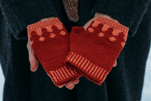 Load image into Gallery viewer, Red knitted fingerless gloves with a pattern held by a person wearing a dark coat.