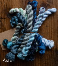 Load image into Gallery viewer, Collection of blue and green yarn skeins on a wooden surface with 'Aster' label.