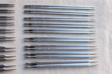 Load image into Gallery viewer, A set of metal knitting needles laid out on a light fabric background, with some needles grouped on the left side. The needles are silver-toned with printed size and brand markings.