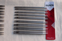 Load image into Gallery viewer, A set of metallic knitting needles arranged on a light fabric background next to a red and white ChiaoGoo Quads packaging card.