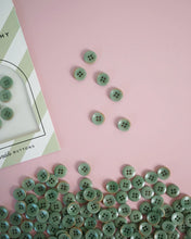 Load image into Gallery viewer, Green buttons scattered on a pink surface with a card labeled 'Buttons' in the corner.