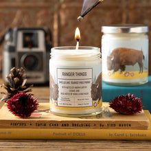 Load image into Gallery viewer, Candle labeled &#39;Ranger Things&#39; with a lit wick, surrounded by decorative items on a wooden surface.