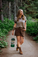 Woman walking on a trail in a forest holding a green lantern.