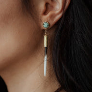 Close-up of an ear wearing a unique earring with a turquoise gemstone and gold accents.