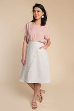 Load image into Gallery viewer, Woman wearing a pink top and white skirt against a beige background