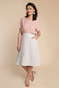Woman wearing a pink top and white skirt against a beige background