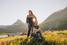 Load image into Gallery viewer, Two people standing on a grassy hill with mountains and a house in the background.