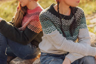 Two people sitting outdoors wearing patterned sweaters.