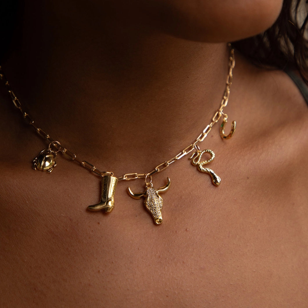 Gold necklace with boot and bull head charm on a person's neck